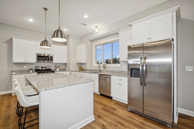 kitchen featuring a center island, a breakfast bar, stainless steel appliances, white cabinetry, and wood finished floors