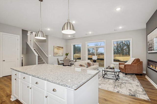 kitchen with a glass covered fireplace, wood finished floors, a center island, light stone countertops, and recessed lighting