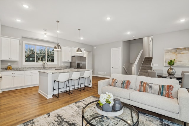 living room with baseboards, stairway, light wood-type flooring, and recessed lighting