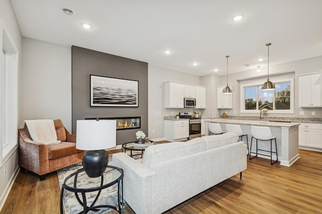 living room featuring a glass covered fireplace, light wood-style flooring, baseboards, and recessed lighting