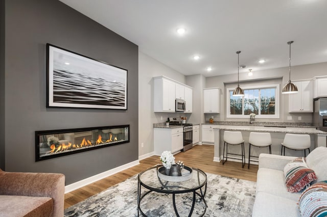 living room with a glass covered fireplace, light wood-style flooring, baseboards, and recessed lighting