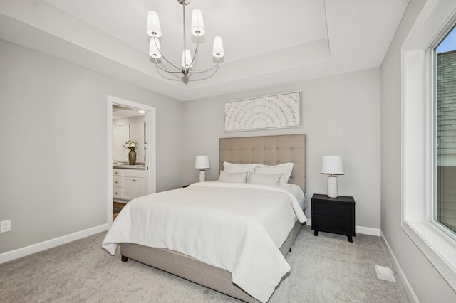 carpeted bedroom featuring a tray ceiling, ensuite bath, a chandelier, multiple windows, and baseboards