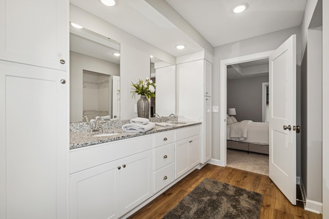 ensuite bathroom featuring a sink, double vanity, wood finished floors, and recessed lighting