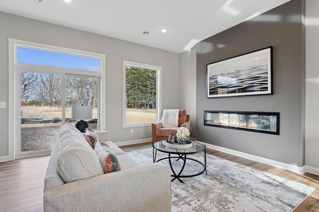 living area featuring a glass covered fireplace, recessed lighting, baseboards, and light wood finished floors