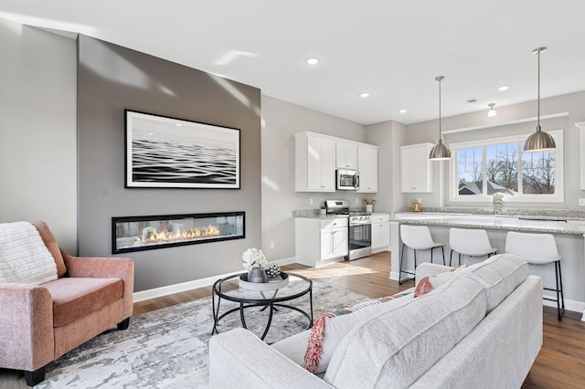 living room featuring recessed lighting, baseboards, a glass covered fireplace, and light wood finished floors