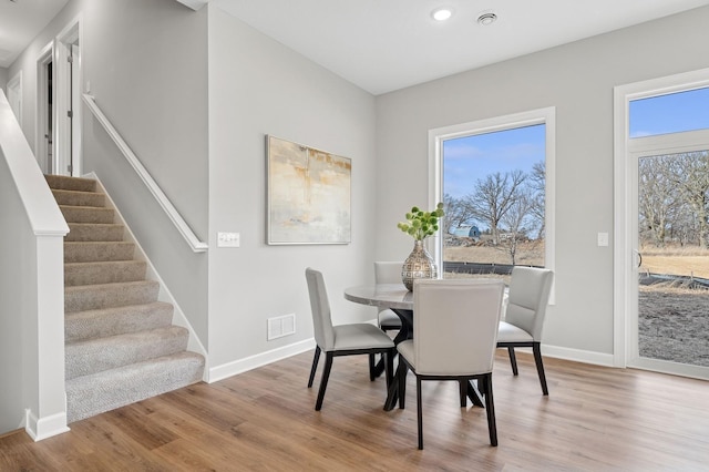 dining space featuring visible vents, baseboards, wood finished floors, and stairs