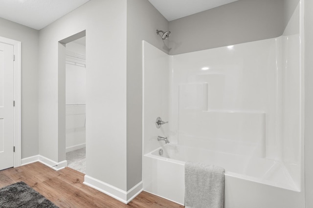 full bathroom with a walk in closet, bathing tub / shower combination, baseboards, and wood finished floors