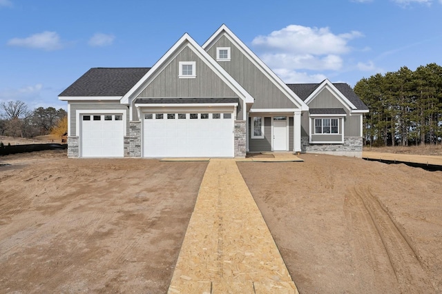 craftsman-style house with stone siding, driveway, and a shingled roof