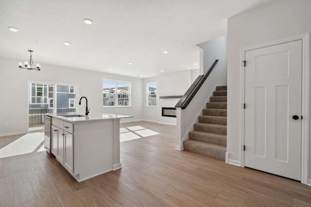 kitchen with pendant lighting, light countertops, open floor plan, a kitchen island with sink, and a sink