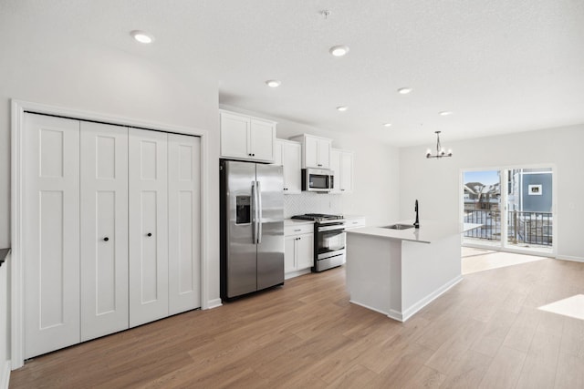 kitchen featuring a kitchen island with sink, white cabinets, light countertops, appliances with stainless steel finishes, and pendant lighting