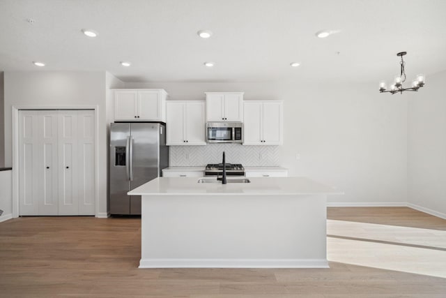 kitchen with appliances with stainless steel finishes, light countertops, white cabinetry, and an island with sink