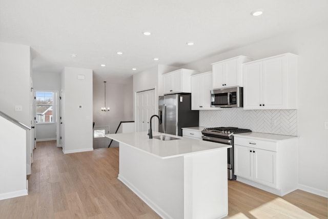 kitchen featuring light countertops, appliances with stainless steel finishes, a kitchen island with sink, a sink, and light wood-type flooring