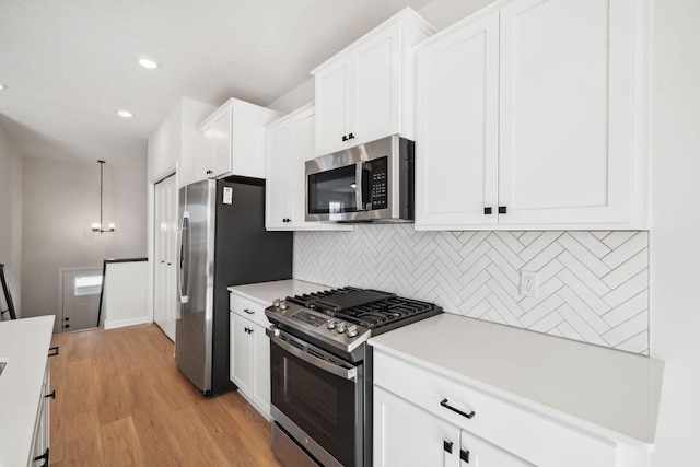 kitchen with white cabinets, light countertops, appliances with stainless steel finishes, backsplash, and decorative light fixtures