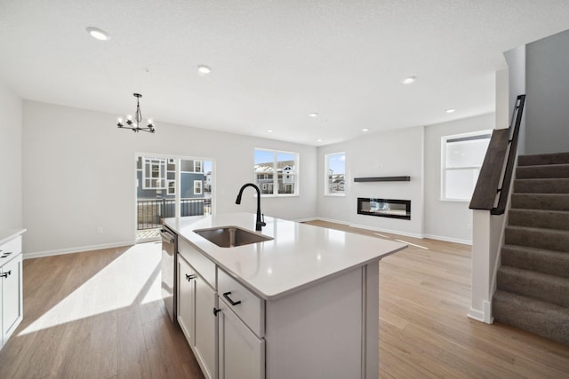 kitchen featuring an island with sink, open floor plan, hanging light fixtures, light countertops, and a sink