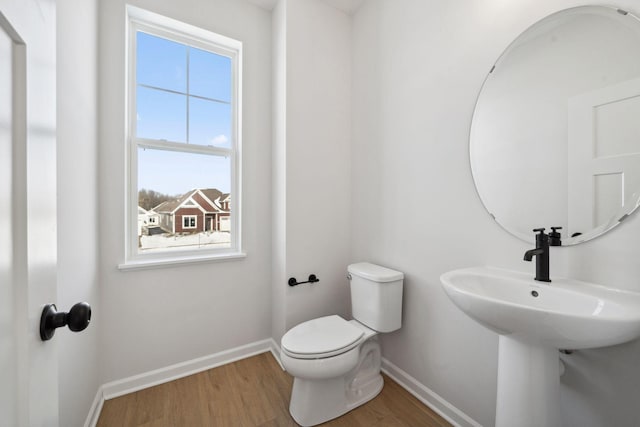 half bath with baseboards, toilet, and wood finished floors