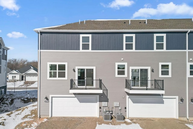 snow covered property with a balcony, an attached garage, and central AC unit