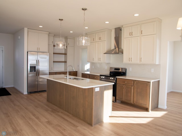 kitchen featuring a center island with sink, stainless steel appliances, light countertops, a sink, and wall chimney range hood