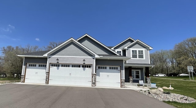 craftsman-style house featuring an attached garage, a front lawn, stone siding, aphalt driveway, and board and batten siding