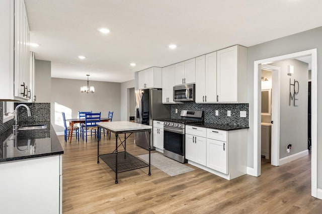 kitchen featuring appliances with stainless steel finishes, white cabinets, a sink, and light wood-style flooring