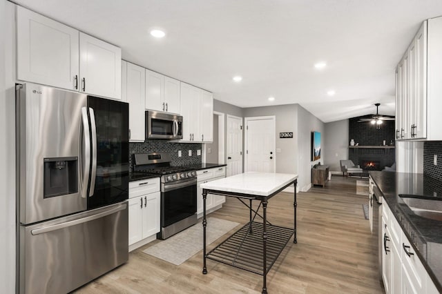 kitchen featuring appliances with stainless steel finishes, a brick fireplace, light wood-style floors, and tasteful backsplash