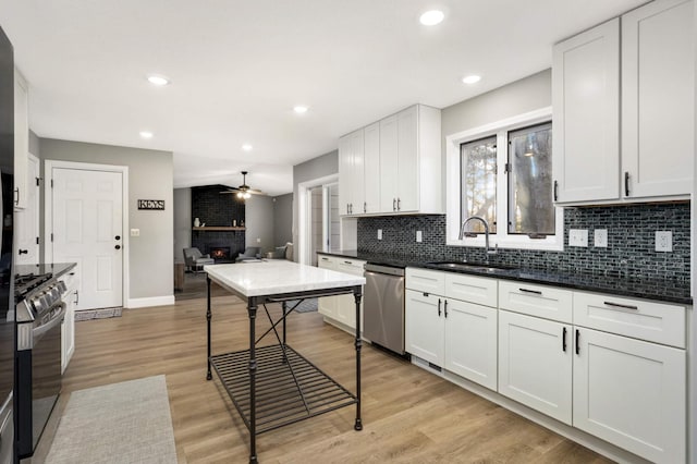 kitchen with decorative backsplash, appliances with stainless steel finishes, light wood-style floors, a large fireplace, and a sink