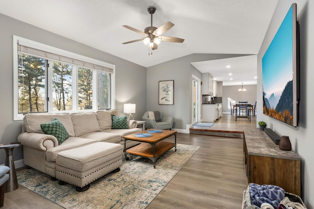 living room with lofted ceiling, ceiling fan with notable chandelier, wood finished floors, and baseboards