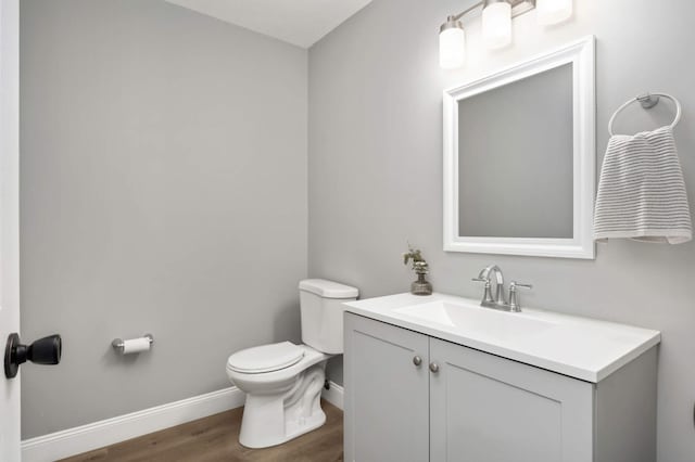 half bathroom with toilet, baseboards, wood finished floors, and vanity