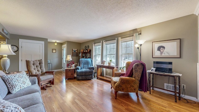 living room with a textured ceiling, light wood-type flooring, visible vents, and baseboards