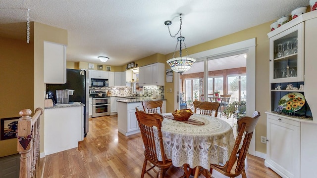 dining space with light wood-style floors, a textured ceiling, and baseboards