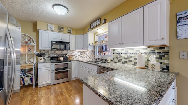 kitchen featuring light wood finished floors, stainless steel appliances, white cabinets, a sink, and dark stone countertops