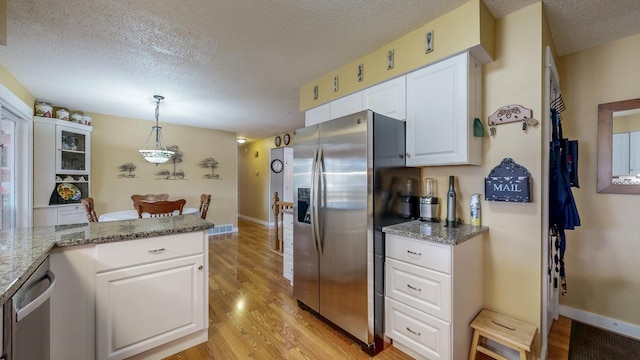 kitchen featuring stainless steel appliances, white cabinetry, light stone countertops, light wood finished floors, and decorative light fixtures