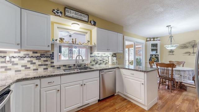 kitchen featuring pendant lighting, light wood finished floors, white cabinetry, a sink, and dishwasher