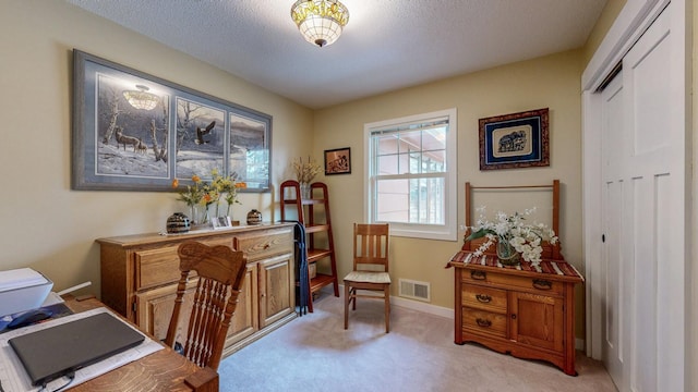 office area with a textured ceiling, baseboards, visible vents, and light colored carpet