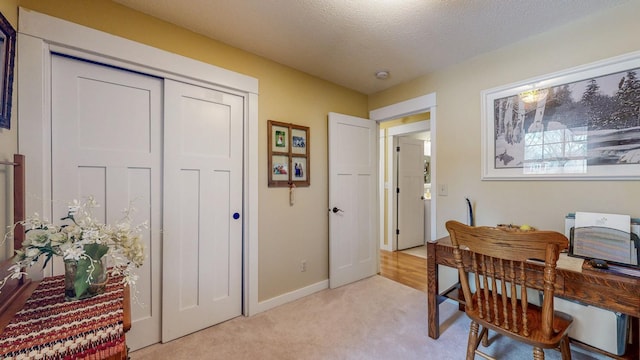 office featuring a textured ceiling, baseboards, and light colored carpet