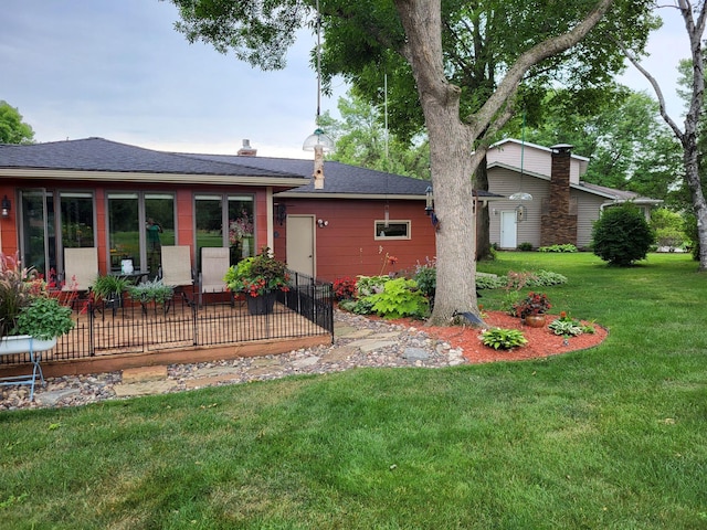 rear view of property with a shingled roof, a yard, and a chimney