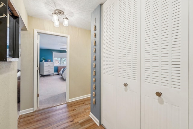 hall featuring wood finished floors, baseboards, and a textured ceiling