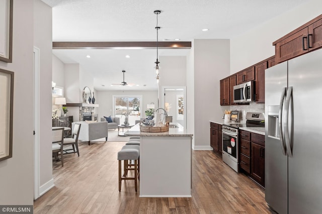 kitchen featuring light wood-style flooring, a fireplace, stainless steel appliances, and a kitchen breakfast bar