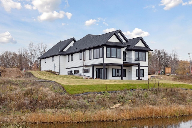 rear view of property with roof with shingles, a lawn, and a balcony