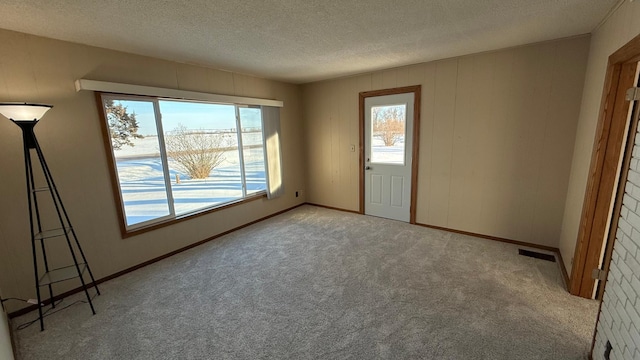 unfurnished room featuring visible vents, light colored carpet, a textured ceiling, and baseboards