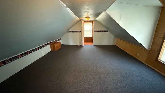 bonus room with lofted ceiling, dark carpet, and wood walls