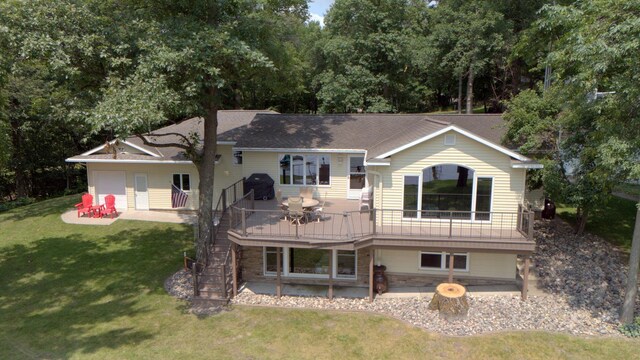 rear view of house featuring a deck, an attached garage, stone siding, a lawn, and a patio area