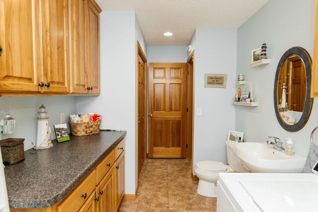 full bathroom with a textured ceiling, a sink, toilet, and baseboards