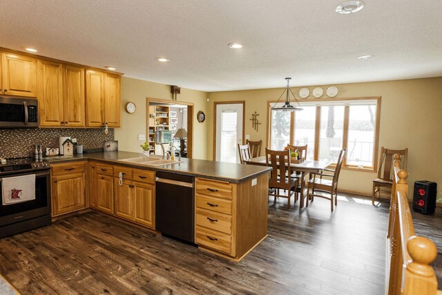 kitchen with a peninsula, dark countertops, pendant lighting, and stainless steel appliances