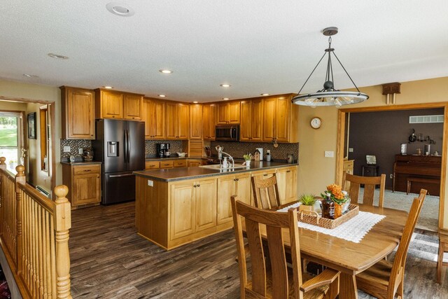 kitchen with stainless steel refrigerator with ice dispenser, brown cabinets, dark countertops, dark wood finished floors, and pendant lighting