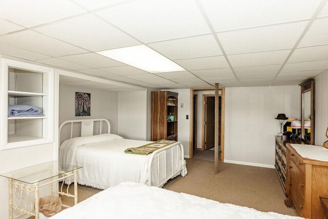 carpeted bedroom featuring a drop ceiling and baseboards