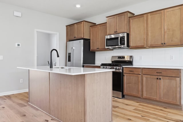 kitchen with a center island with sink, light wood finished floors, decorative backsplash, appliances with stainless steel finishes, and a sink