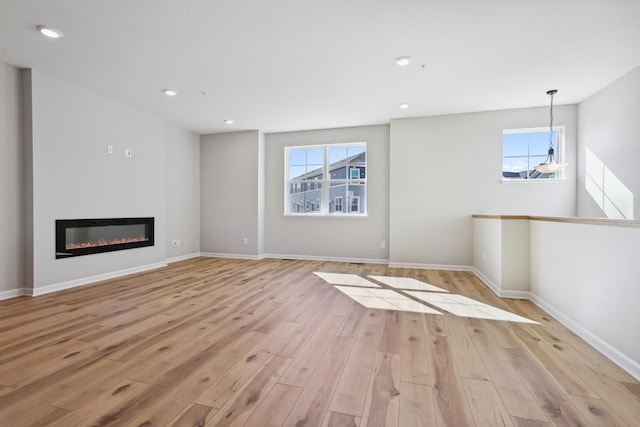 unfurnished living room with recessed lighting, light wood-type flooring, a glass covered fireplace, and a healthy amount of sunlight