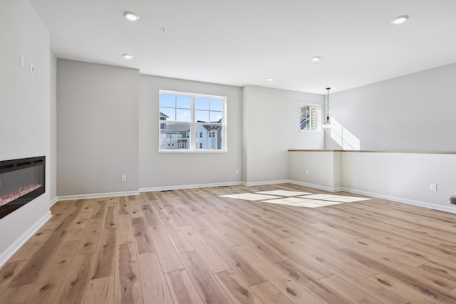 unfurnished living room with baseboards, a glass covered fireplace, light wood-style flooring, and a healthy amount of sunlight