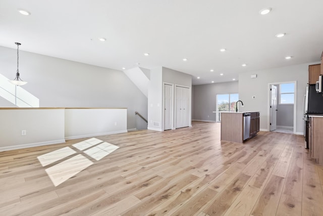 kitchen with light wood-style flooring, a sink, open floor plan, an island with sink, and pendant lighting