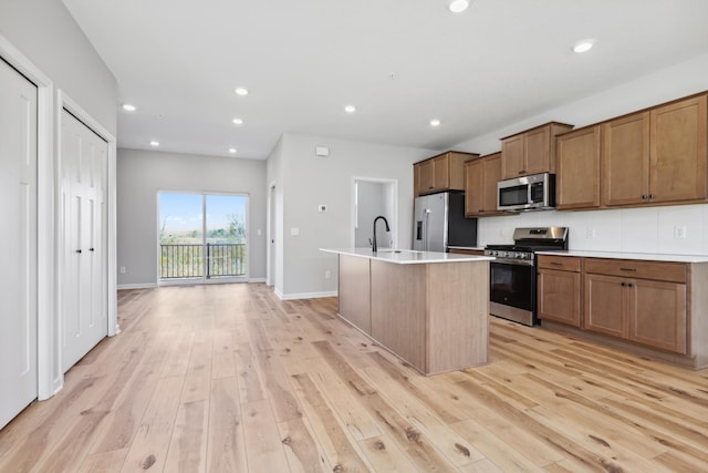 kitchen with a center island with sink, light wood finished floors, recessed lighting, appliances with stainless steel finishes, and brown cabinetry